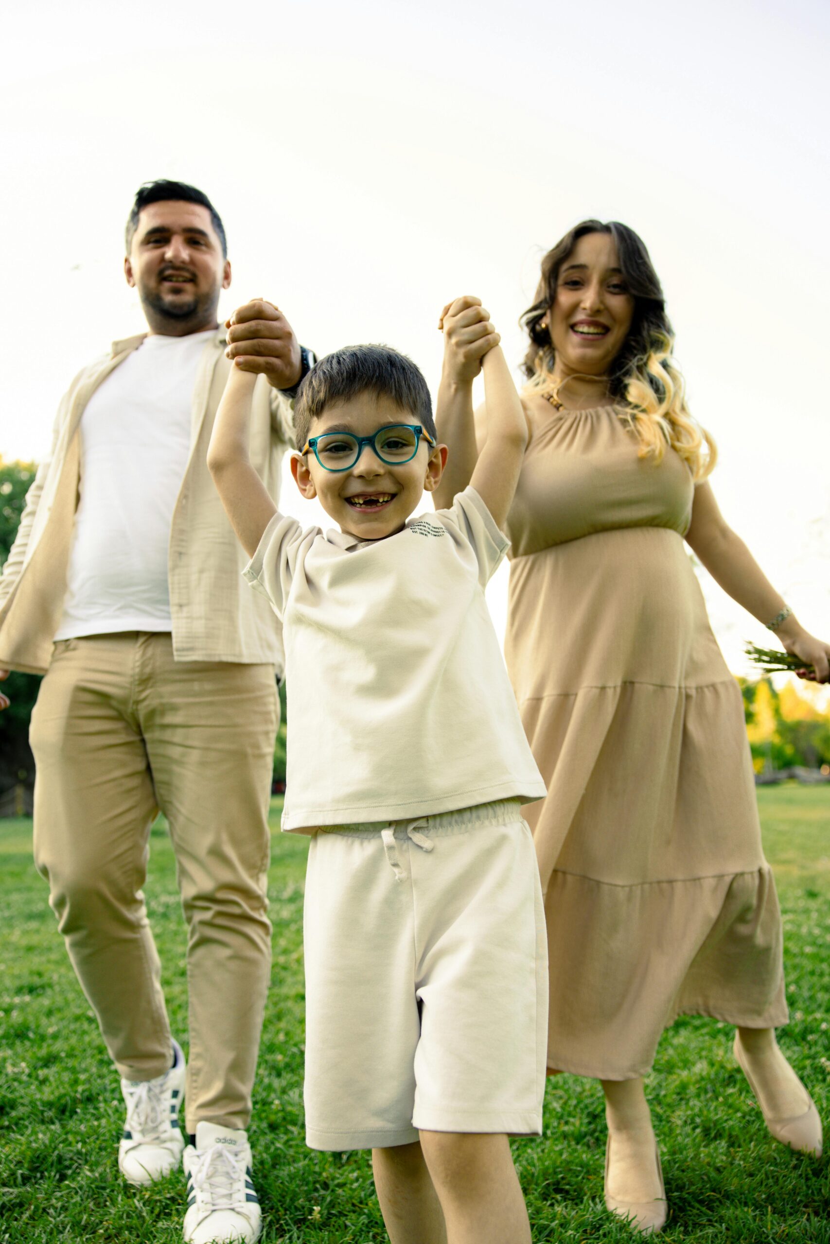 About A joyful family moment with parents and child holding hands outdoors during a sunny day.