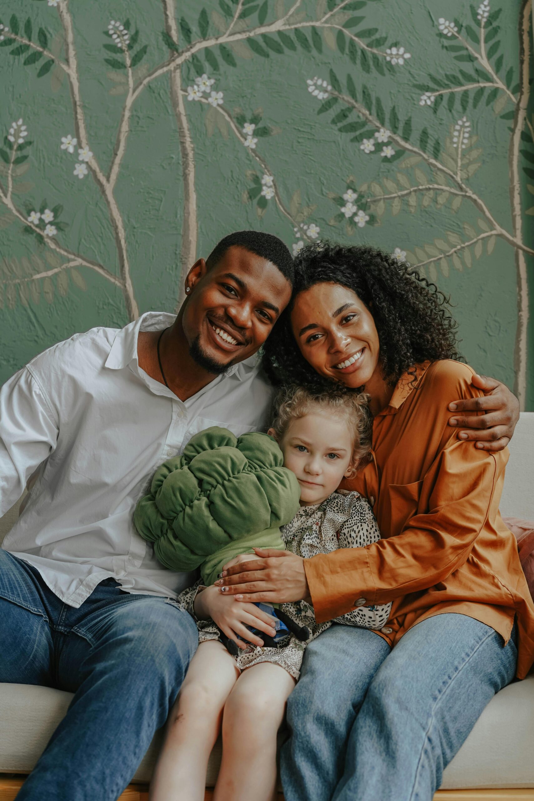 About A cheerful family of three with a child hugging on a sofa indoors.